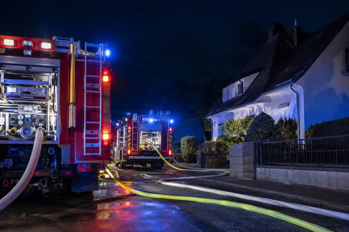 Wozy strażackie i węże gaśnicze przy domu jednorodzinnym nocą