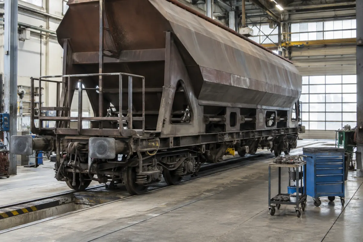 Wagon towarowy stojący w hali naprawczej obok stanowiska z narzędziami